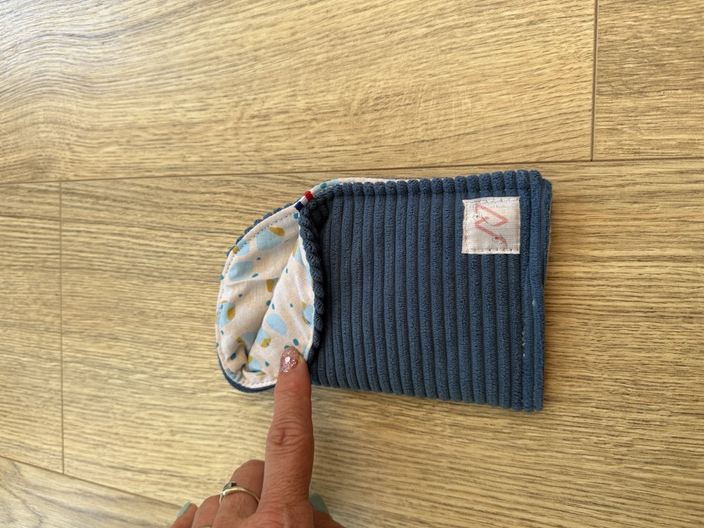 Étui à lunettes bleu gris entrouvert à la main, détail de la doublure écrue à pois bleus et moutarde