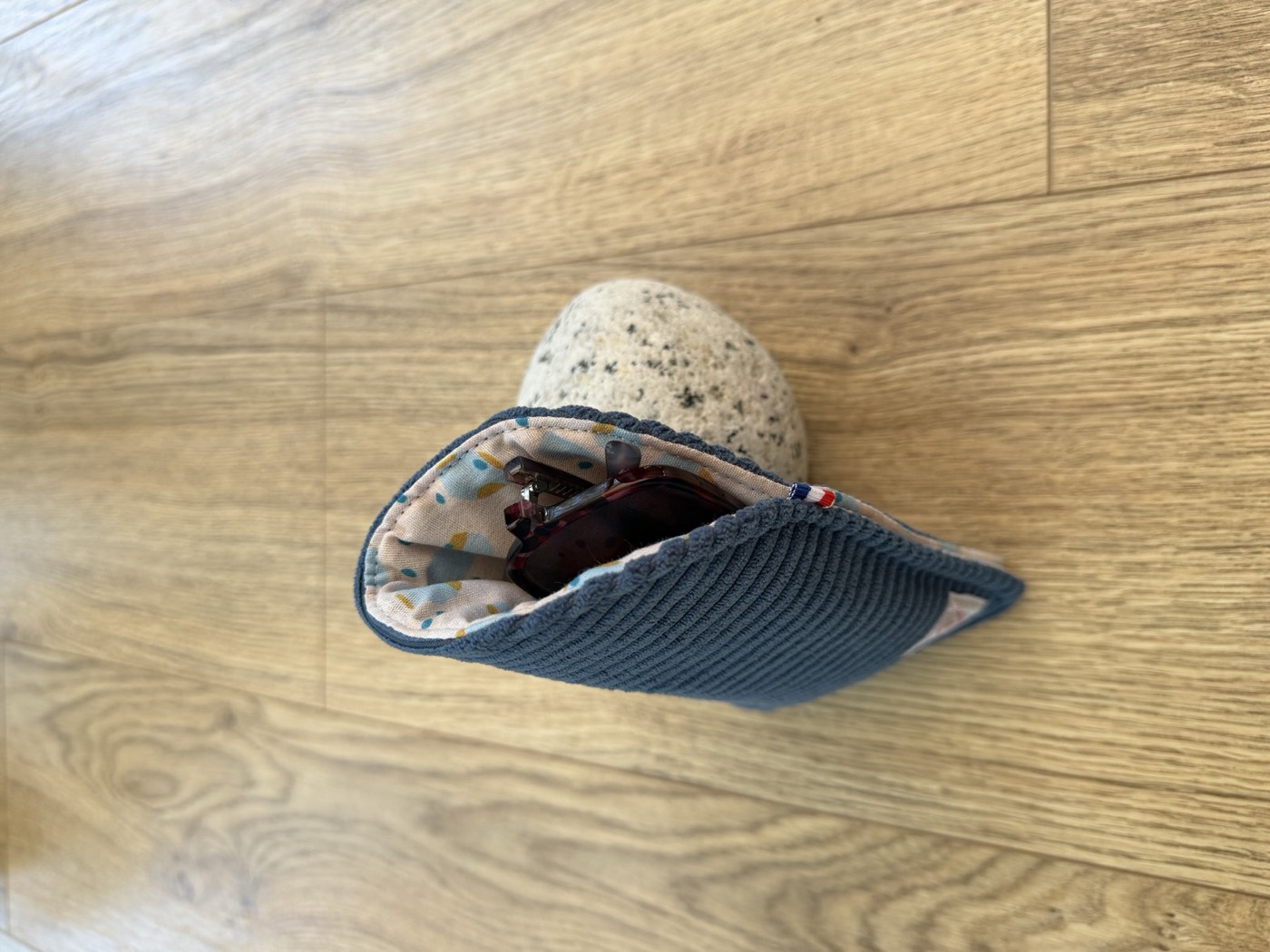 Étui à lunettes bleu gris ouvert, doublure écrue à pois bleus et moutarde, avec une paire de lunettes