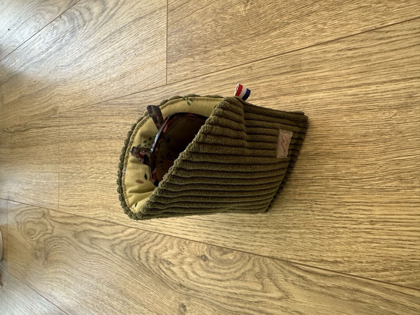 Étui à lunettes kaki ouvert, doublure jaune pâle à sapins, avec une paire de lunettes
