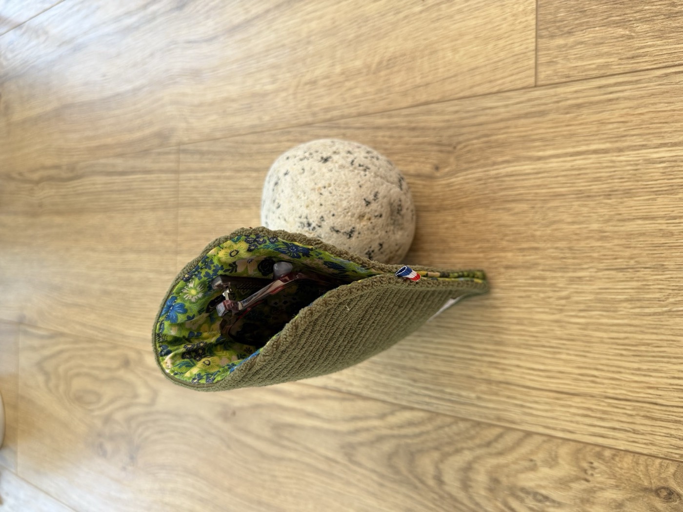 Étui à lunettes ouvert, doublure fleurie verte et bleue, avec une paire de lunettes