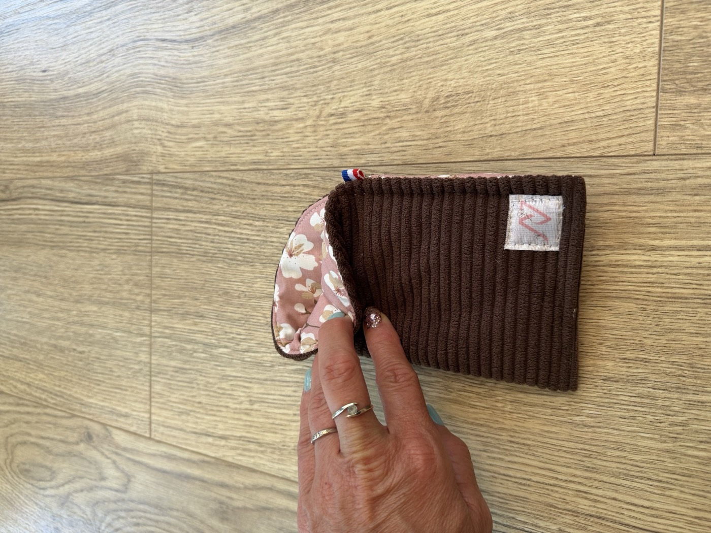 Étui à lunettes marron entrouvert à la main, détail de la doublure rose poudré à fleurs