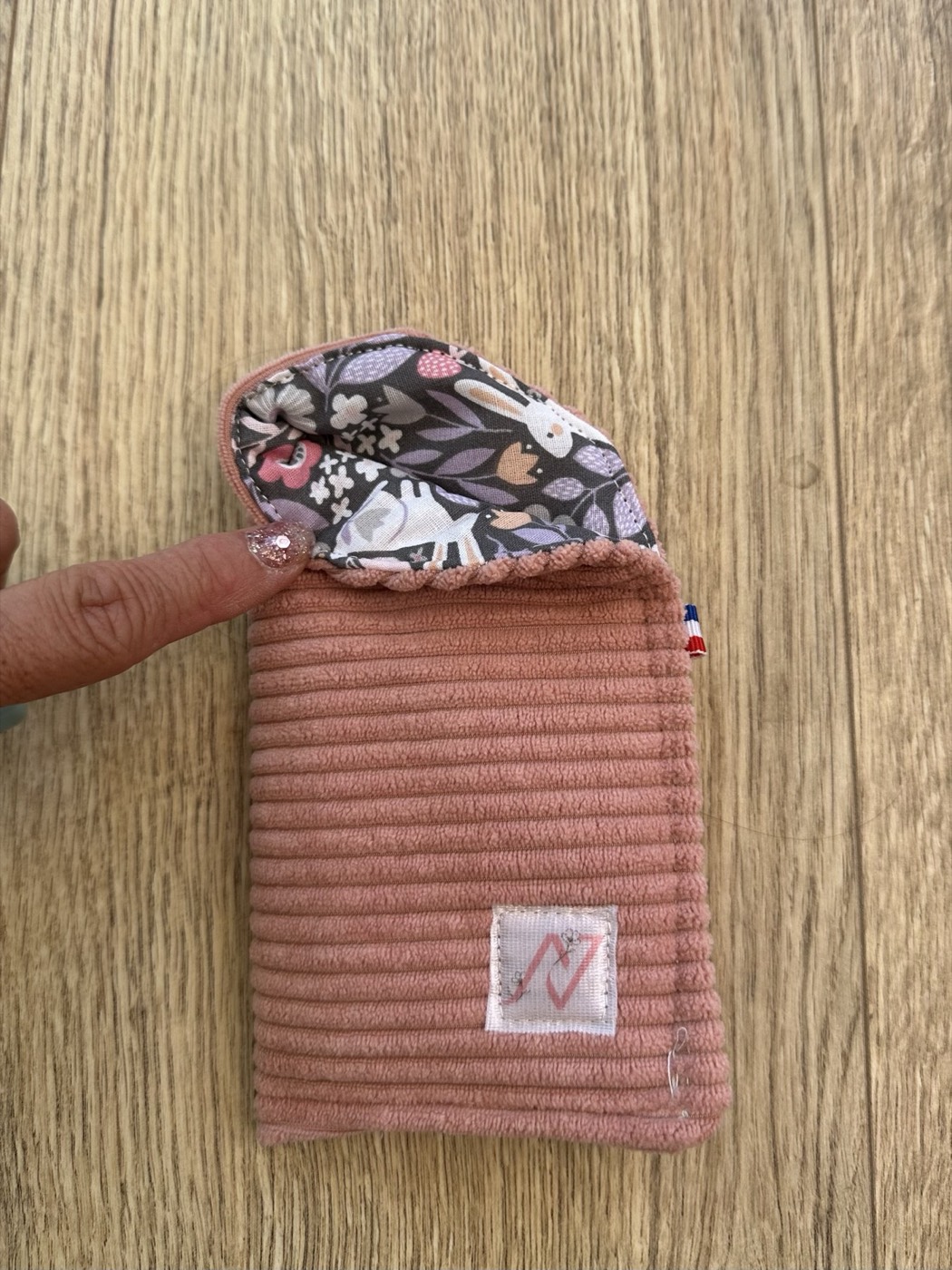 Étui à lunettes rose entrouvert à la main, détail de la doublure grise à lapins et fleurs
