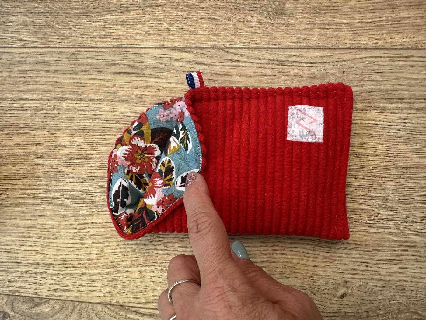 Étui à lunettes rouge entrouvert à la main, détail de la doublure fleurie bleue et rouge