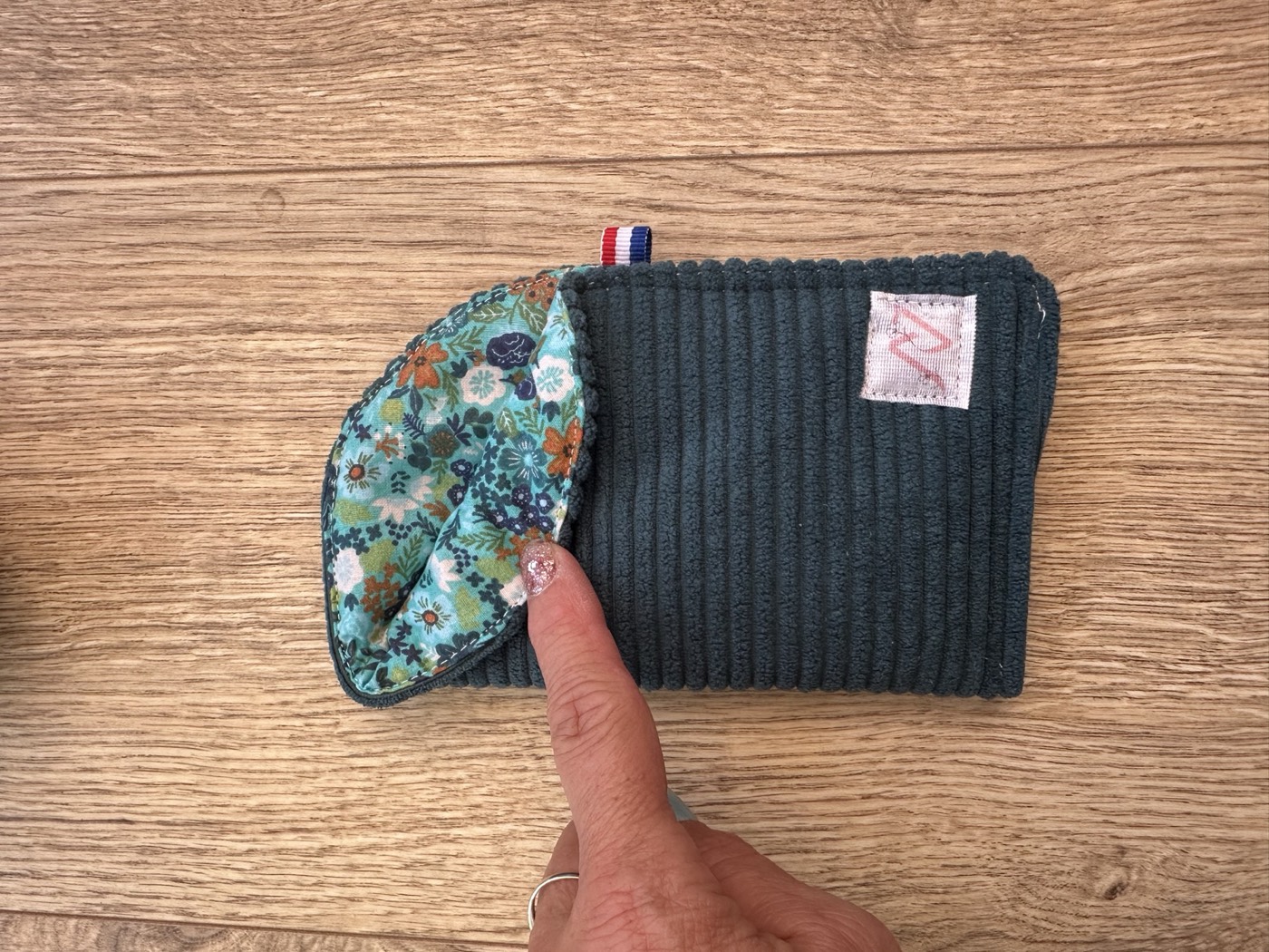 Étui à lunettes vert bouteille entrouvert à la main, détail de la doublure fleurie turquoise