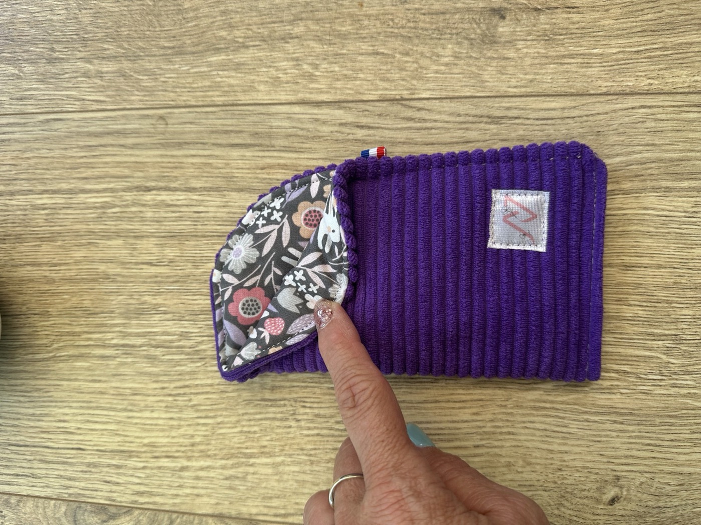 Étui à lunettes violet entrouvert à la main, détail de la doublure grise à fleurs roses