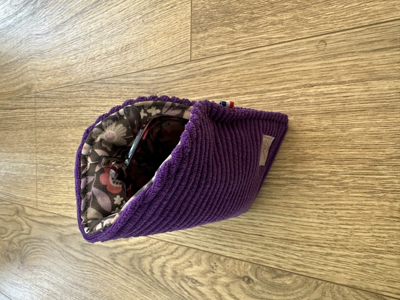 Étui à lunettes violet ouvert, doublure grise à fleurs roses, avec une paire de lunettes